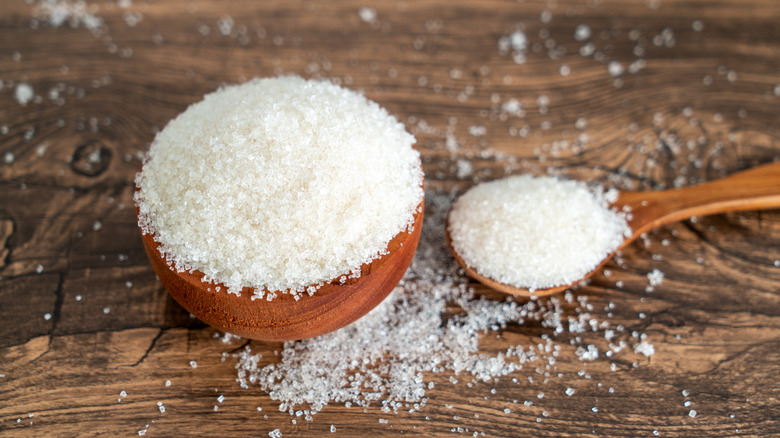 Granulated sugar in wooden bowl by spoonful of sugar