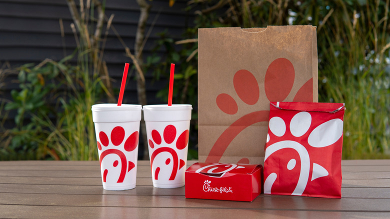 Chick-fil-A logo bags, box, and two styrofoam cups with straws on wooden table
