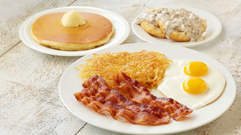 Plates of eggs, bacon, and hashbrowns, a pancake, and a biscuit with white gravy