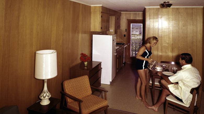 A woman serves coffee to a man in a wood-paneled kitchen